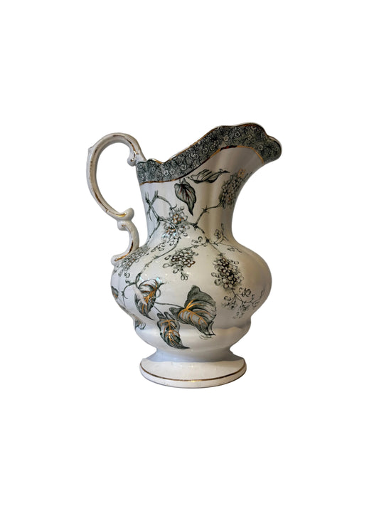 Floral pitcher with leaf motifs, patterned rim, curved handle and footed base